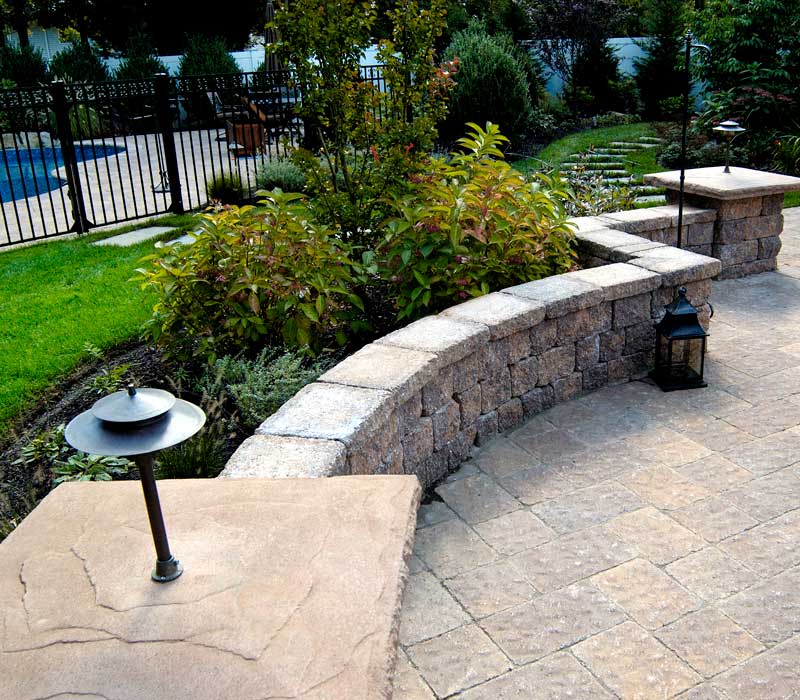 Curved retaining wall with greenery and pool in background