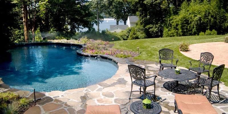 Kidney pool overlooking a lake with outdoor table and chairs